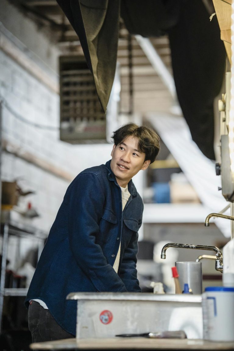 Man in a workshop wearing a blue jacket, engaged in industrial work.